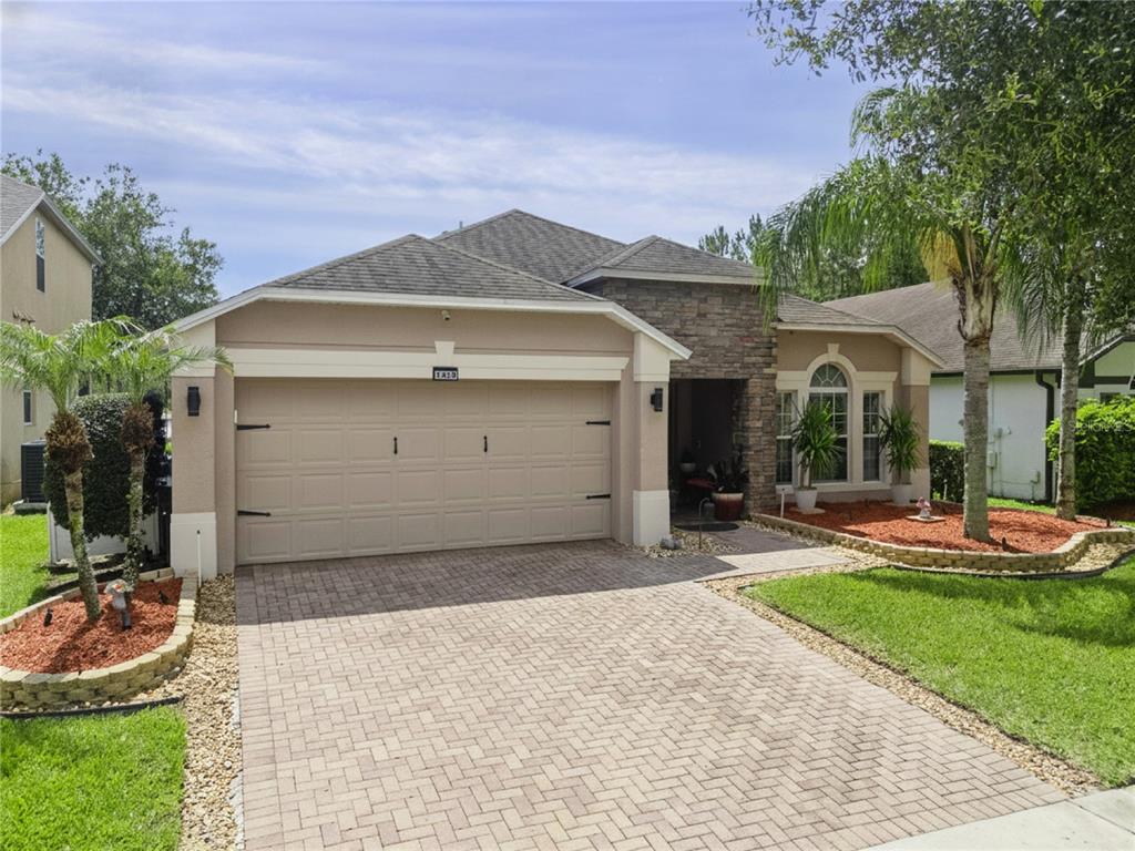 A single-story house with a beige stucco exterior, stone accents, and a paved driveway — 1519 BALSAM WILLOW TRAIL, ORLANDO, FL