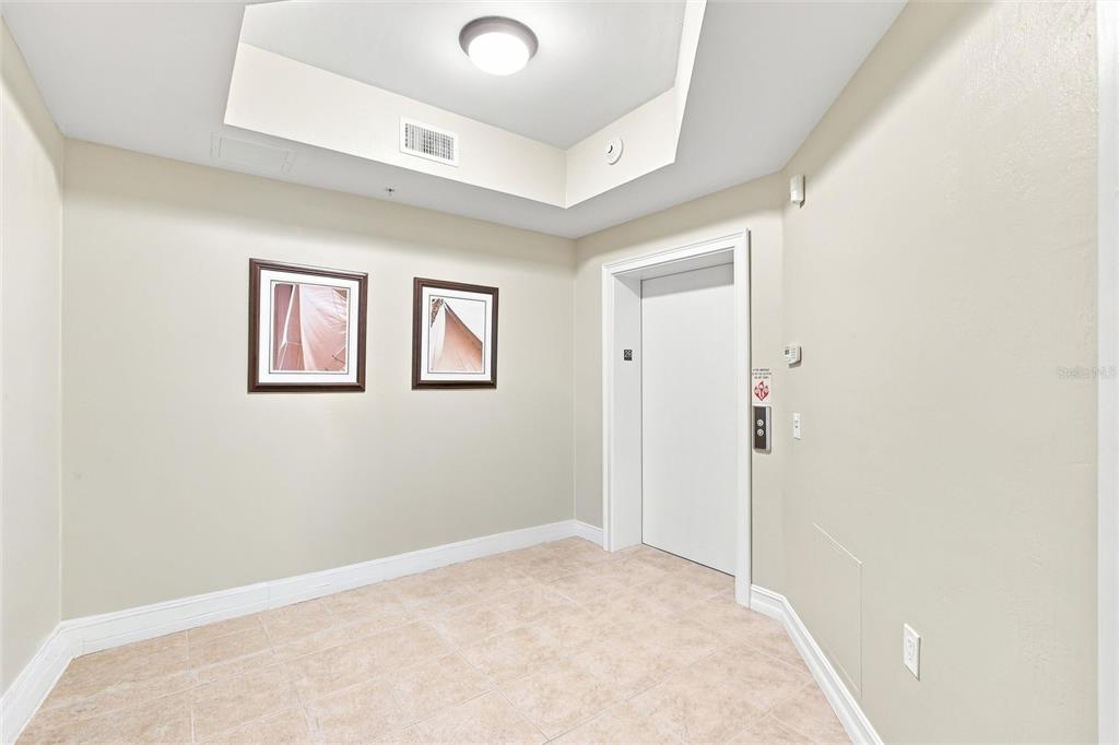 An elevator lobby with beige tile flooring, a tray ceiling, and two framed wall pictures — 87 VIVANTE BOULEVARD UNIT 206, PUNTA GORDA, FL