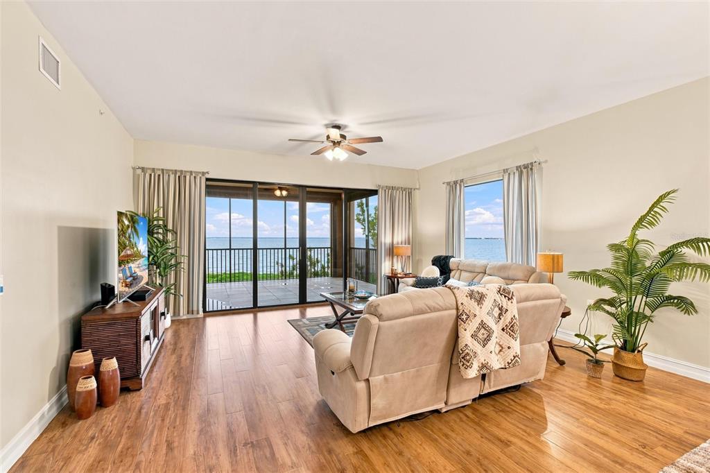 A living room with wood flooring, a beige sofa, and sliding glass doors overlooking water — 87 VIVANTE BOULEVARD UNIT 206, PUNTA GORDA, FL