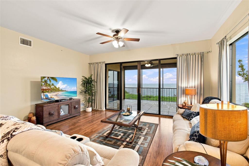 A living room with a television, ceiling fan, and sliding glass doors overlooking the ocean — 87 VIVANTE BOULEVARD UNIT 206, PUNTA GORDA, FL