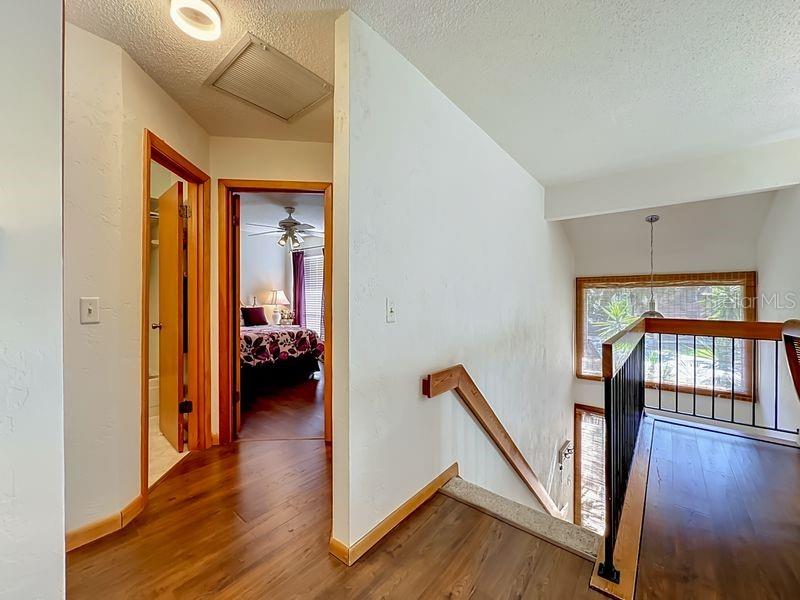 A hallway with wood flooring leads to a bedroom, with a staircase and railing nearby — 10 OAKMONT COURT UNIT 10, PALM COAST, FL