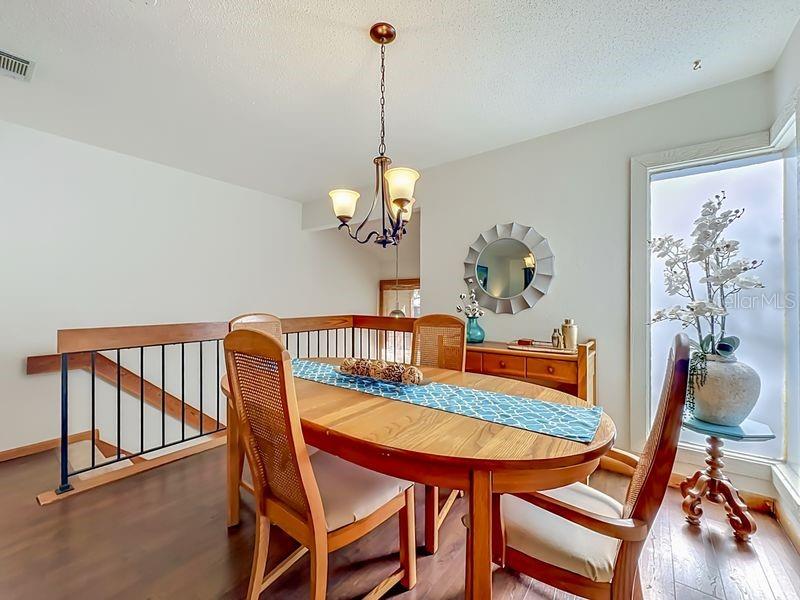 A dining area features a wooden table, chairs, a chandelier, and a staircase railing — 10 OAKMONT COURT UNIT 10, PALM COAST, FL