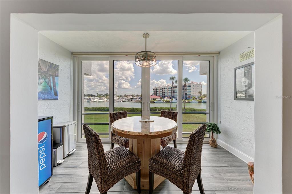 A dining area features a round wooden table, wicker chairs, and sliding glass doors overlooking water — 250 SANTA MARIA STREET UNIT 219, VENICE, FL