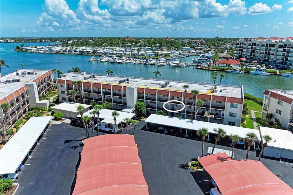 An aerial view shows a multi-story apartment building with covered parking and a nearby marina — 250 SANTA MARIA STREET UNIT 219, VENICE, FL