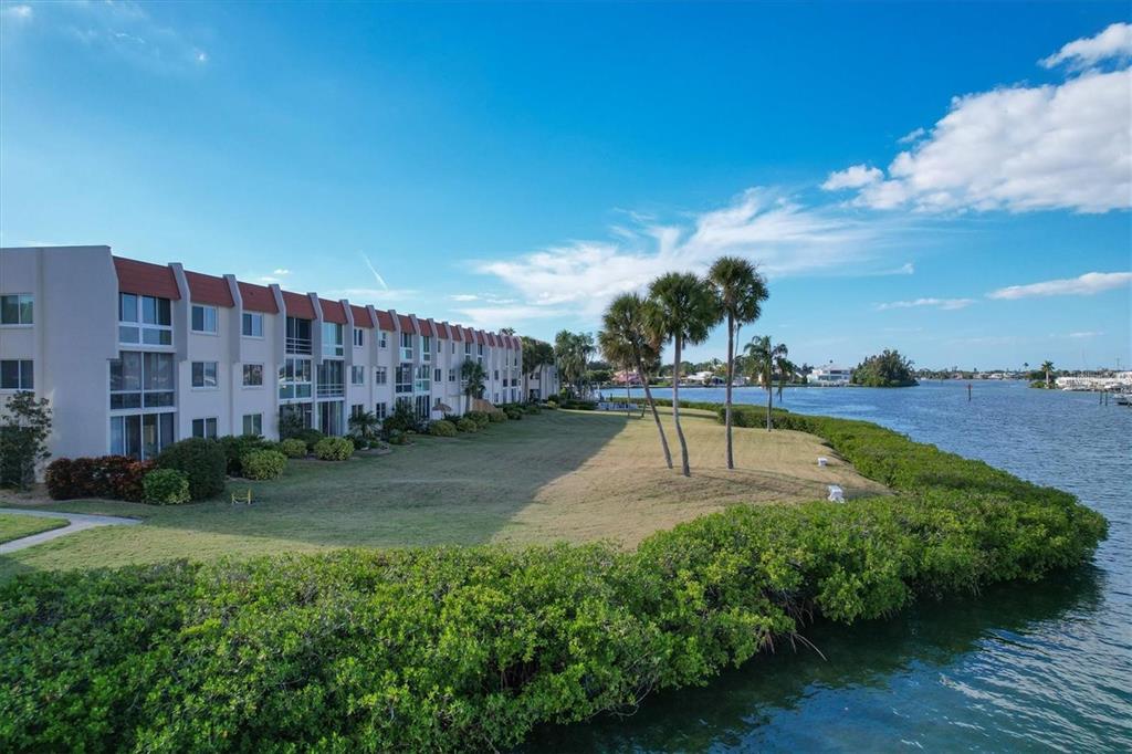 An exterior view of a multi-story apartment building situated along a waterfront with palm trees — 250 SANTA MARIA STREET UNIT 219, VENICE, FL