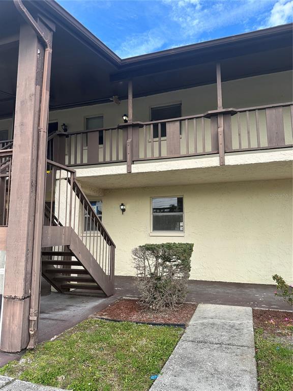 A two-story building features a wooden staircase leading to an upper balcony with railings — 8440 OLD POST ROAD UNIT 202, PORT RICHEY, FL
