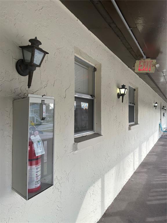 An exterior view of a building wall featuring a fire extinguisher cabinet and wall lamps — 8440 OLD POST ROAD UNIT 202, PORT RICHEY, FL