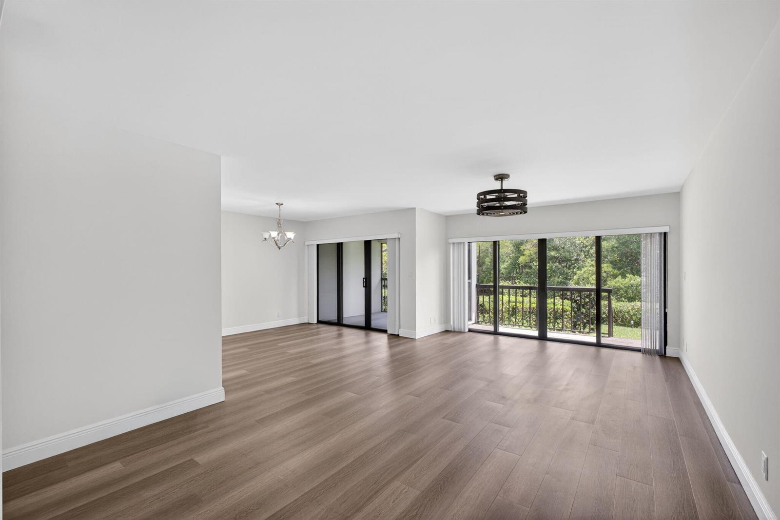 An empty living area features wood-look flooring, white walls, and two sets of sliding glass doors — 2104 Fairway Drive S, Jupiter FL 33477, JUPITER, FL