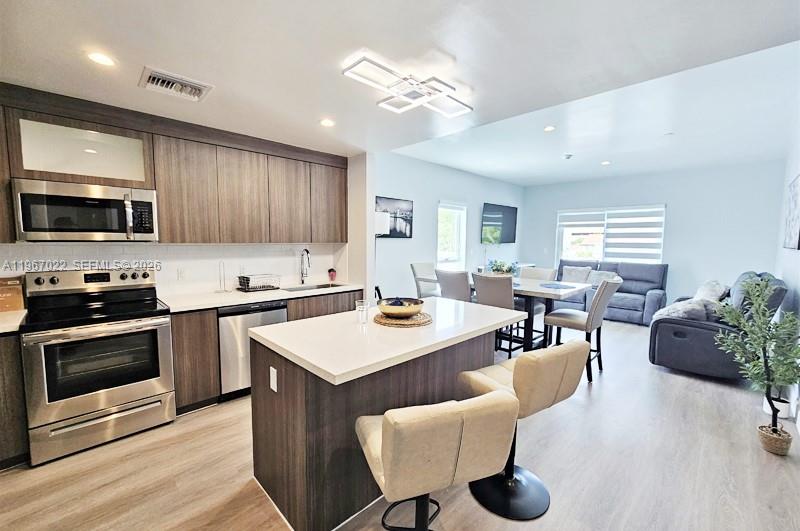 A modern kitchen with wood cabinets and a white island opens into a living area — 1938 Jackson St # 202, Hollywood FL 33020, HOLLYWOOD, FL
