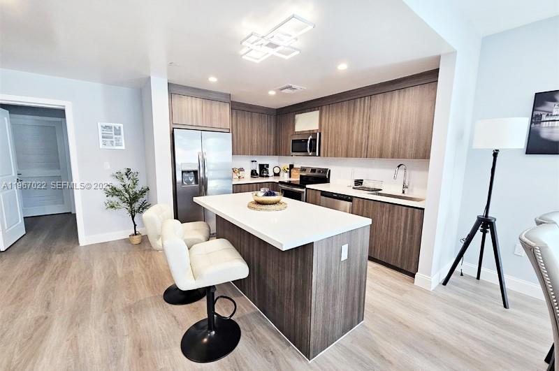 A modern kitchen features wood-grain cabinetry, a white quartz island, and stainless steel appliances — 1938 Jackson St # 202, Hollywood FL 33020, HOLLYWOOD, FL