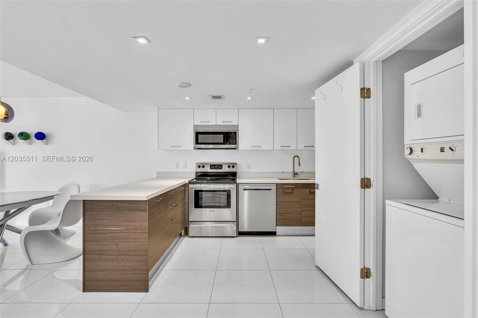 A modern kitchen features white upper cabinets, wood-tone lower cabinets, stainless appliances, and tile flooring — 9901 E Bay Harbor Dr # 802, Bay Harbor Islands FL 33154, BAY HARBOR ISLANDS, FL