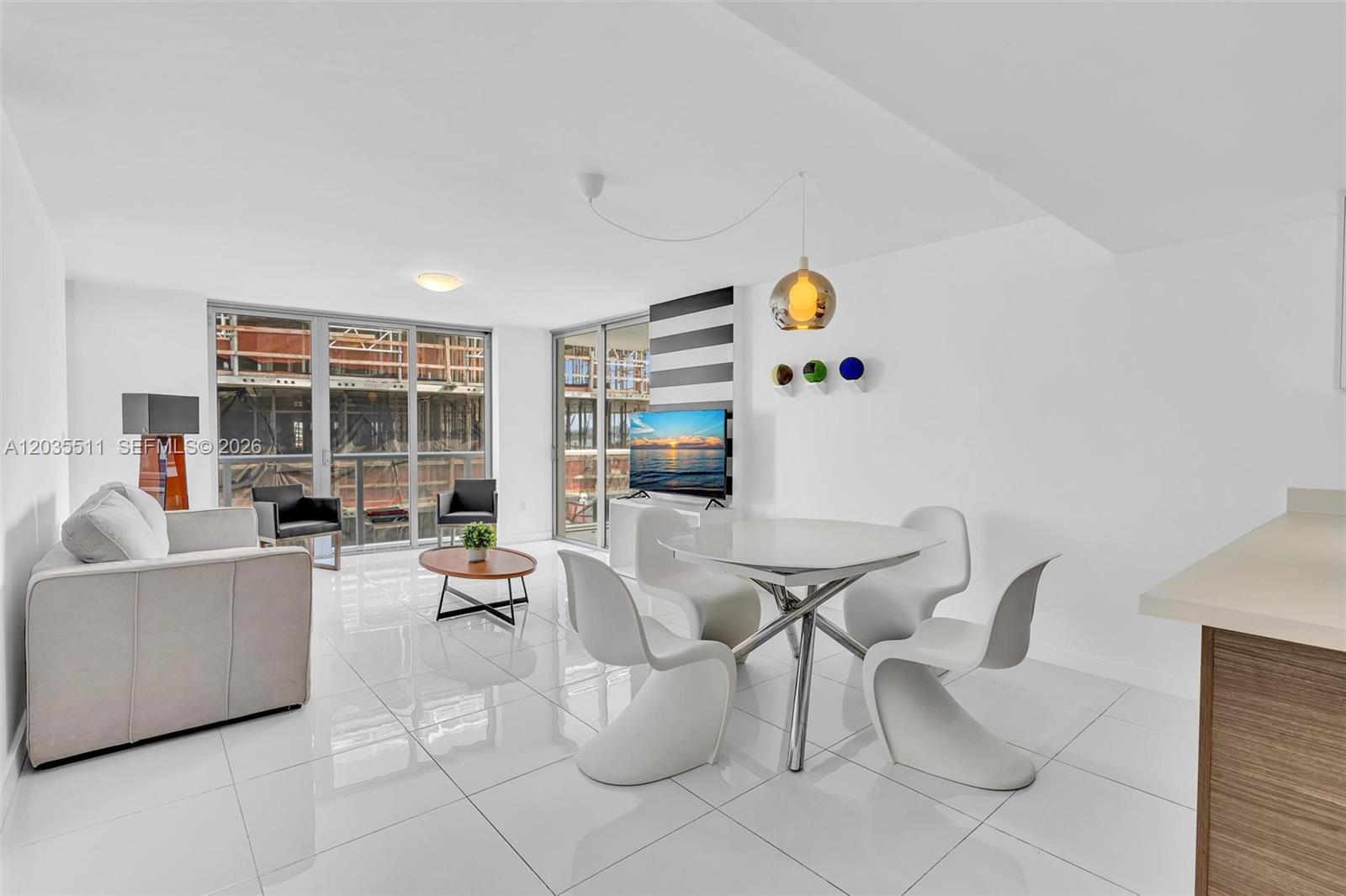 A modern living and dining area features white tile floors, contemporary furniture, and floor-to-ceiling windows — 9901 E Bay Harbor Dr # 802, Bay Harbor Islands FL 33154, BAY HARBOR ISLANDS, FL