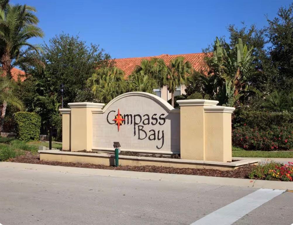 A beige stucco monument sign for Compass Bay stands in front of trees and buildings — 3109 SEAVIEW CASTLE DRIVE, KISSIMMEE, FL
