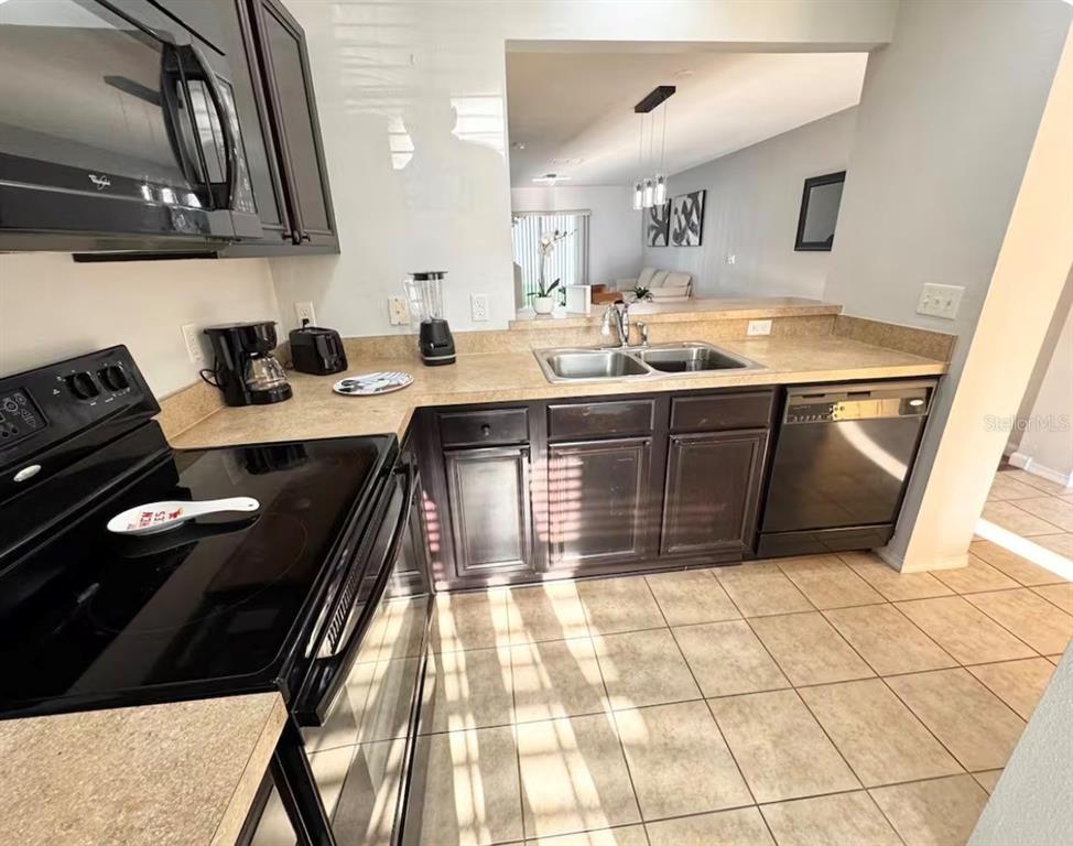 A kitchen features dark wood cabinets, tan countertops, black appliances, and tile flooring — 3109 SEAVIEW CASTLE DRIVE, KISSIMMEE, FL