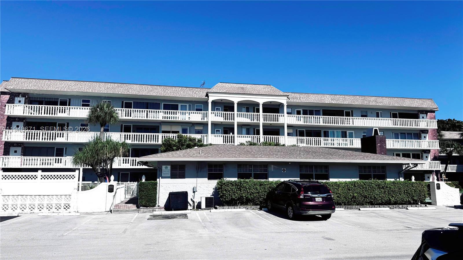 A three-story apartment building with a parking lot in front under a clear blue sky — 1965 SE 5th Ct # 203, Pompano Beach FL 33060, POMPANO BEACH, FL