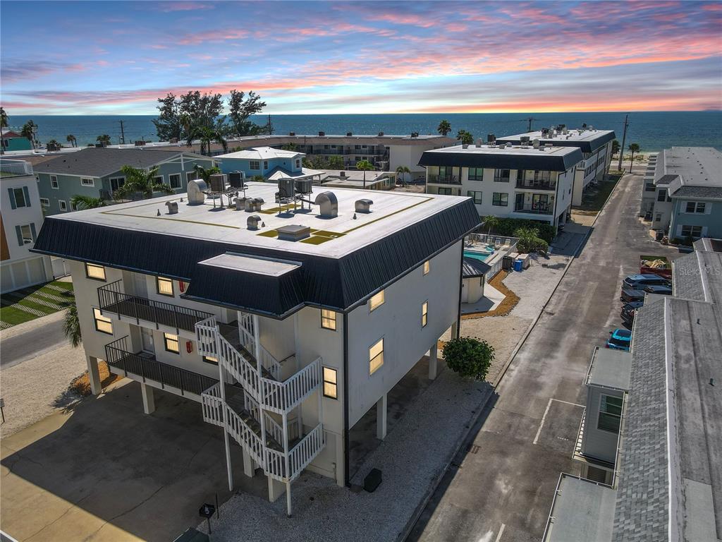 An elevated multi-story apartment building with exterior staircases sits near a beach at sunset — 601 GULF DRIVE N UNIT 109, BRADENTON BEACH, FL
