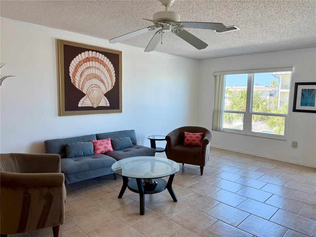 A living room features a grey sofa, two brown armchairs, a glass coffee table, and tile flooring — 601 GULF DRIVE N UNIT 109, BRADENTON BEACH, FL