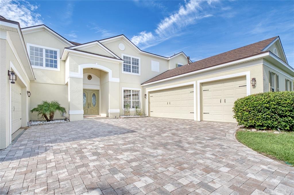 A two-story house with a paved driveway, three garage doors, and a light-colored stucco exterior — 2924 MAJESTIC ISLE DRIVE, CLERMONT, FL