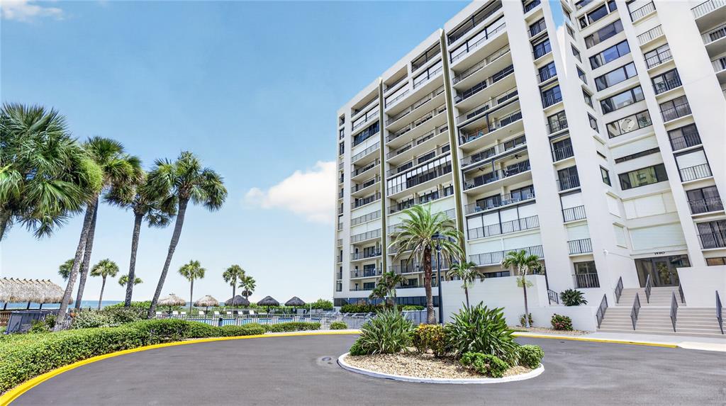A multi-story apartment building stands next to a circular driveway and palm trees — 1480 GULF BOULEVARD UNIT 601, CLEARWATER BEACH, FL