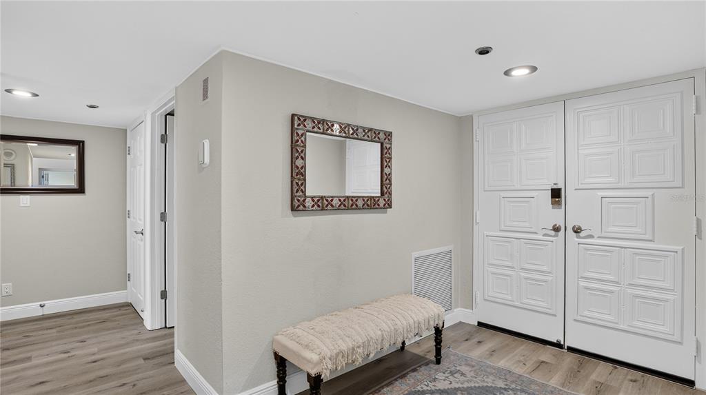 An entryway features a bench, a decorative mirror, and white double doors on wood flooring — 1480 GULF BOULEVARD UNIT 601, CLEARWATER BEACH, FL