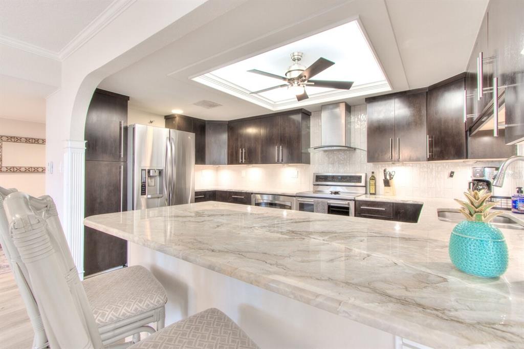 A kitchen features dark wood cabinets, a marble-topped island, and a ceiling fan with lighting — 1480 GULF BOULEVARD UNIT 601, CLEARWATER BEACH, FL