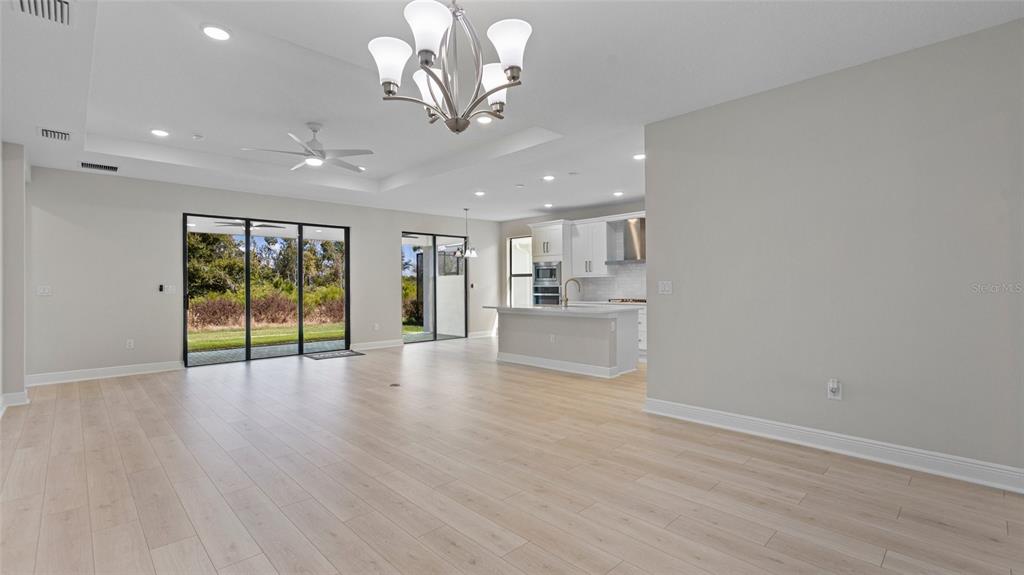 An open-concept living area features light wood floors, a kitchen island, and sliding glass doors — 4984 FAIRHOPE CIRCLE, LAKEWOOD RANCH, FL