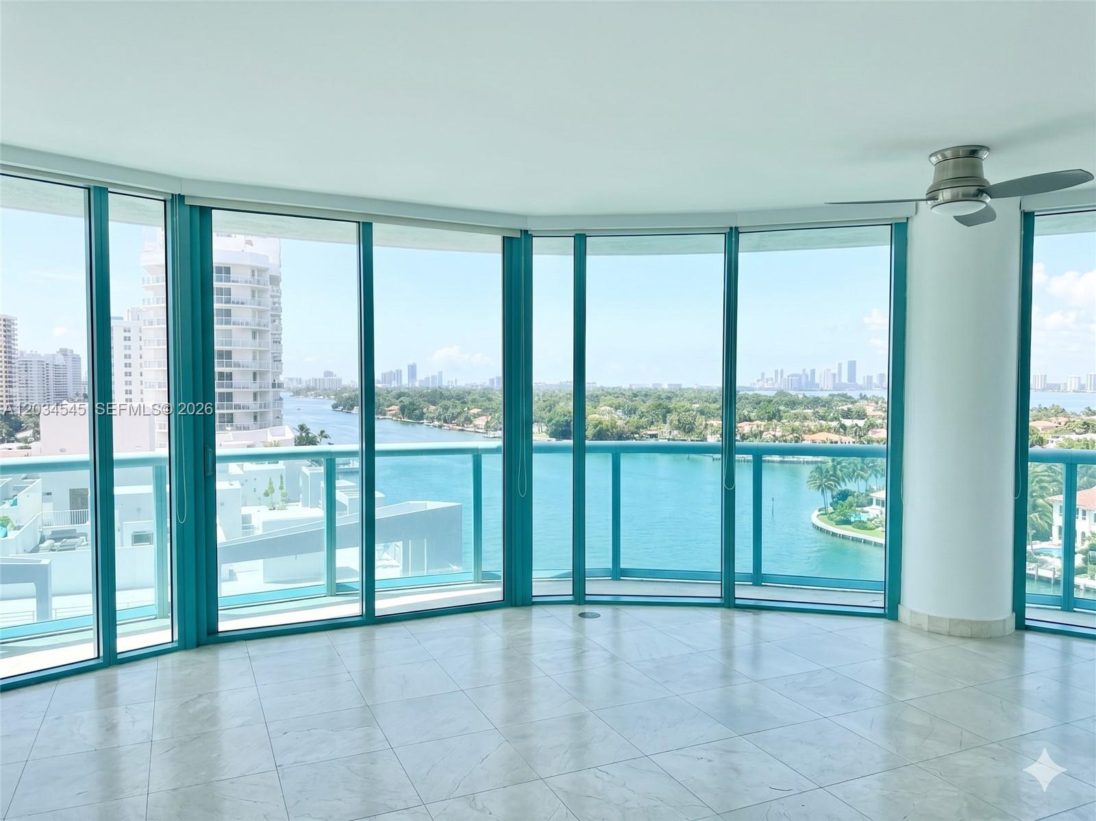 An empty room with light tile flooring features floor-to-ceiling windows overlooking a bay — 6000 Indian Creek Dr # 10A, Miami Beach FL 33140, MIAMI BEACH, FL