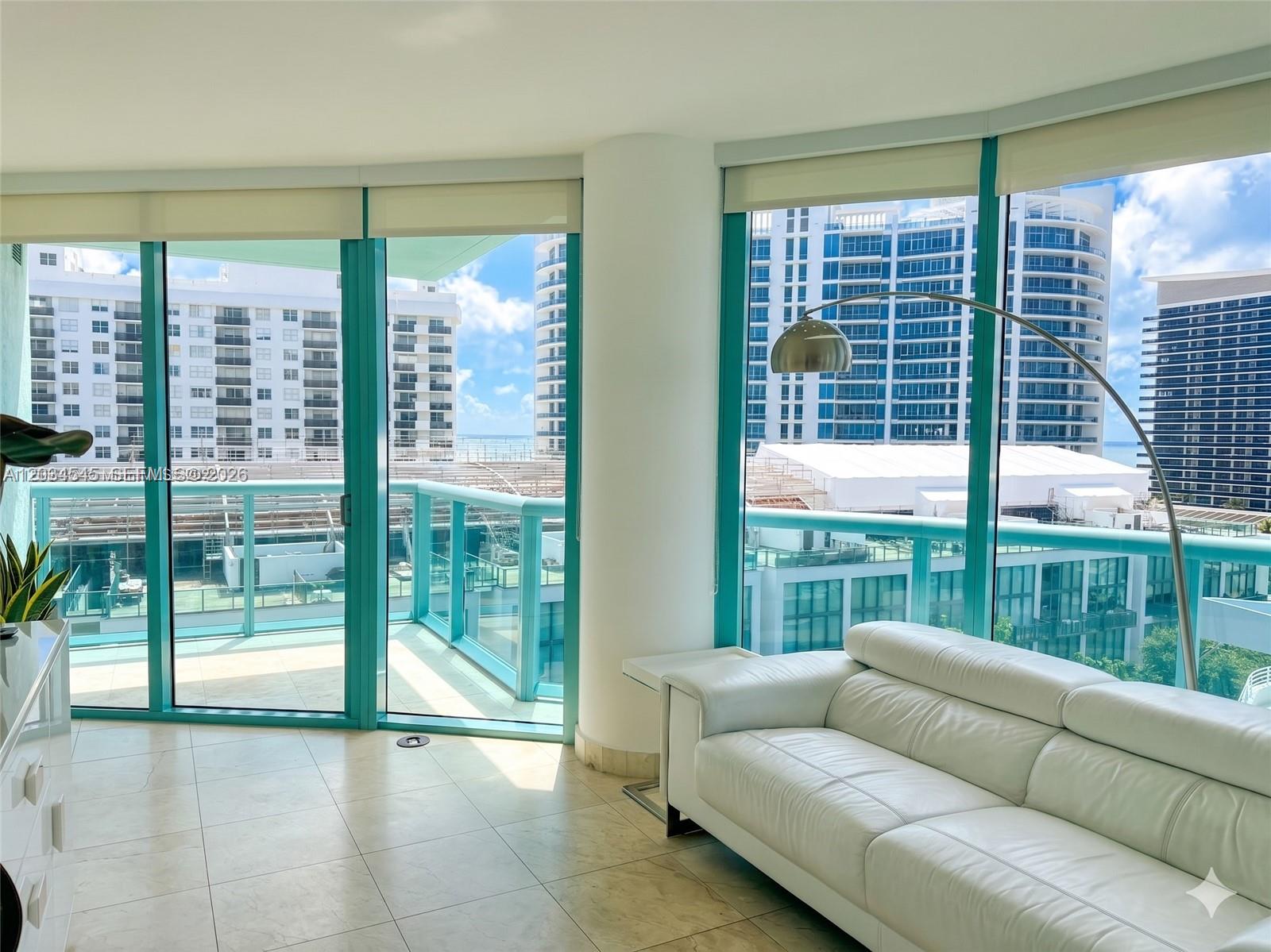 A living room features a white leather sofa, floor-to-ceiling windows, and a balcony overlooking buildings — 6000 Indian Creek Dr # 10A, Miami Beach FL 33140, MIAMI BEACH, FL