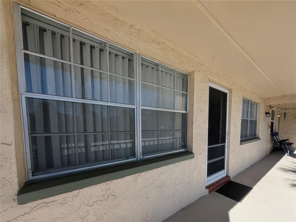 A beige stucco exterior wall features a large window, a screen door, and a walkway — 11620 PARK BOULEVARD UNIT 209, SEMINOLE, FL