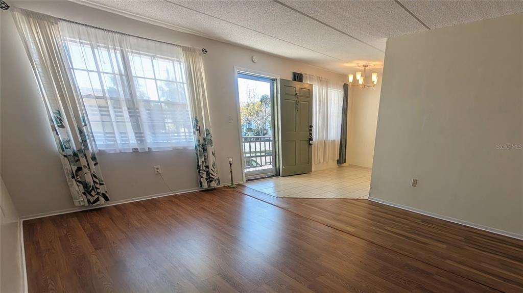 A living room with wood-look flooring, a window with curtains, and an adjacent tiled entryway — 11620 PARK BOULEVARD UNIT 209, SEMINOLE, FL