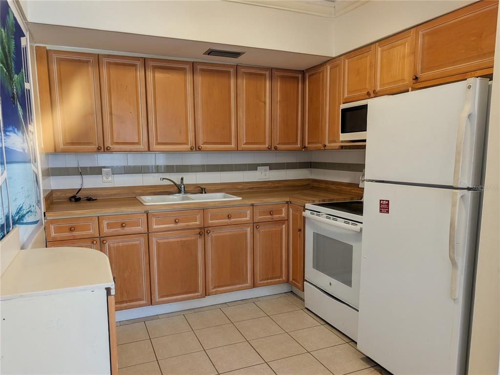 A kitchen features light wood cabinets, laminate countertops, white appliances, and beige tile flooring — 11620 PARK BOULEVARD UNIT 209, SEMINOLE, FL