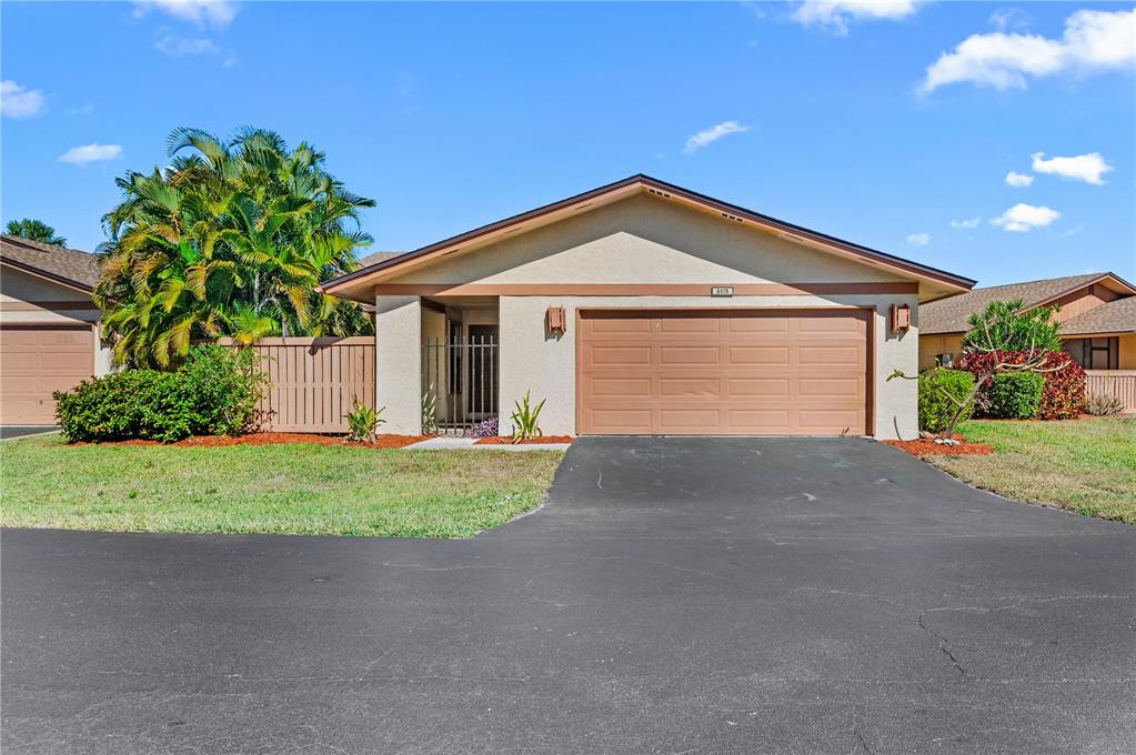 A single-story house with a tan stucco exterior, a two-car garage, and a palm tree — 6479 ROYAL WOODS DRIVE, FORT MYERS, FL