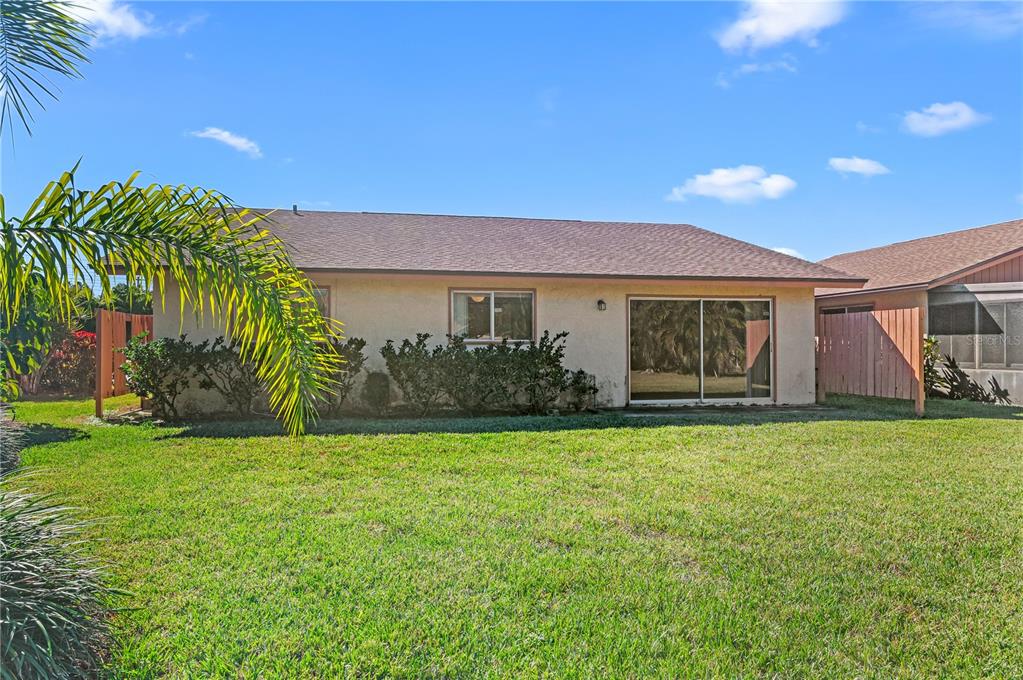 The exterior rear view of a single-story house with a lawn and sliding glass doors — 6479 ROYAL WOODS DRIVE, FORT MYERS, FL