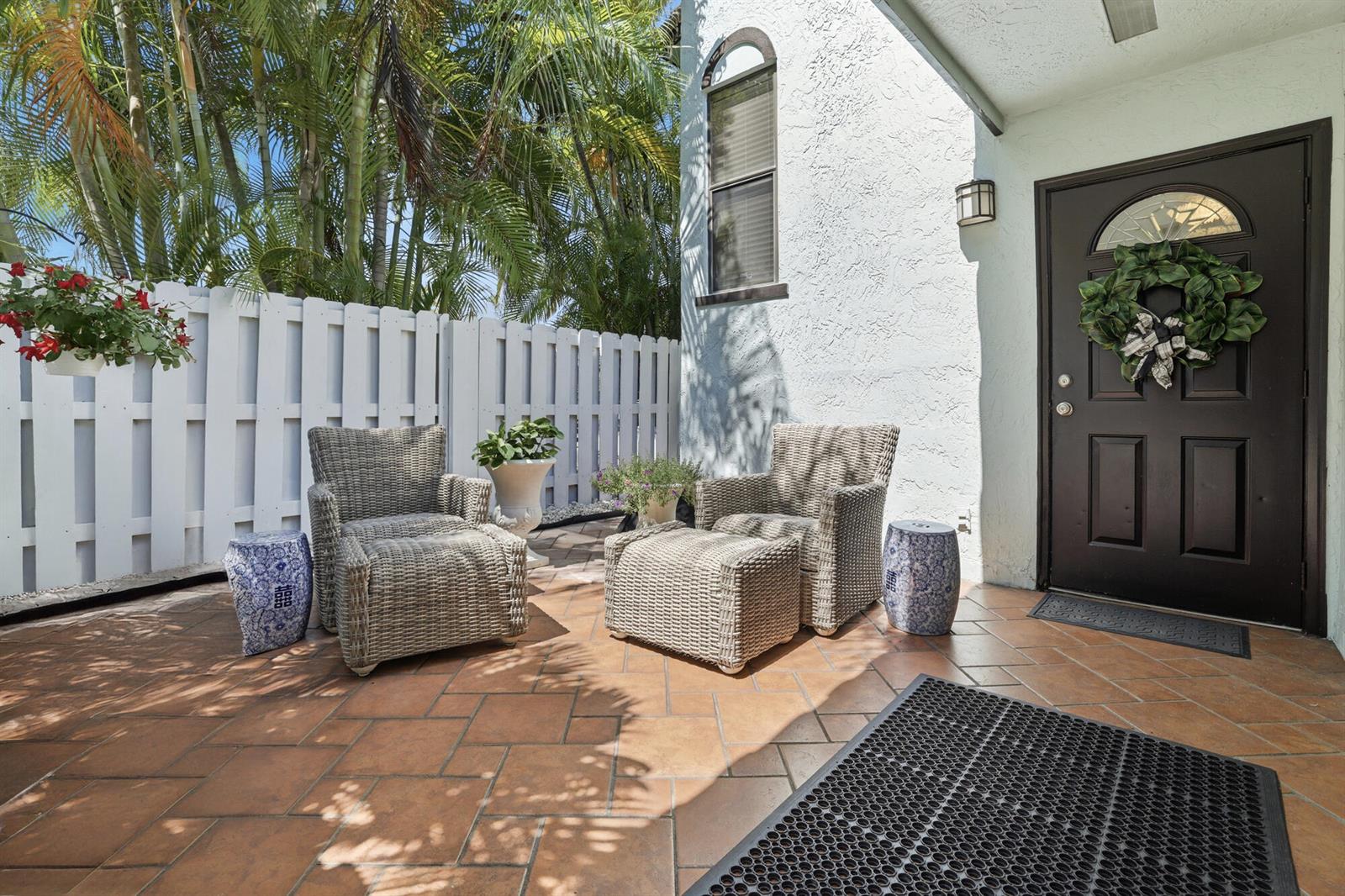 A patio features two wicker chairs with ottomans, blue ceramic stools, and a white fence — 22316 Pineapple Walk Drive, Boca Raton FL 33433, BOCA RATON, FL