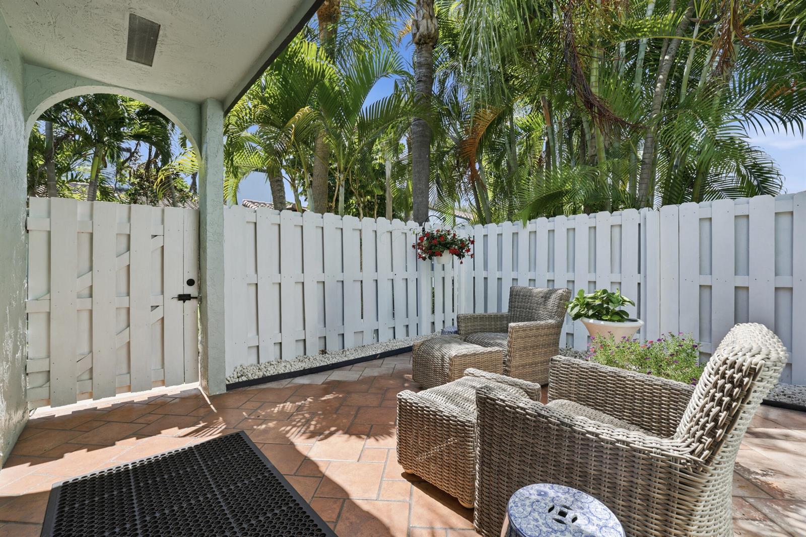 A patio features wicker furniture, a white privacy fence, and palm trees under a blue sky — 22316 Pineapple Walk Drive, Boca Raton FL 33433, BOCA RATON, FL
