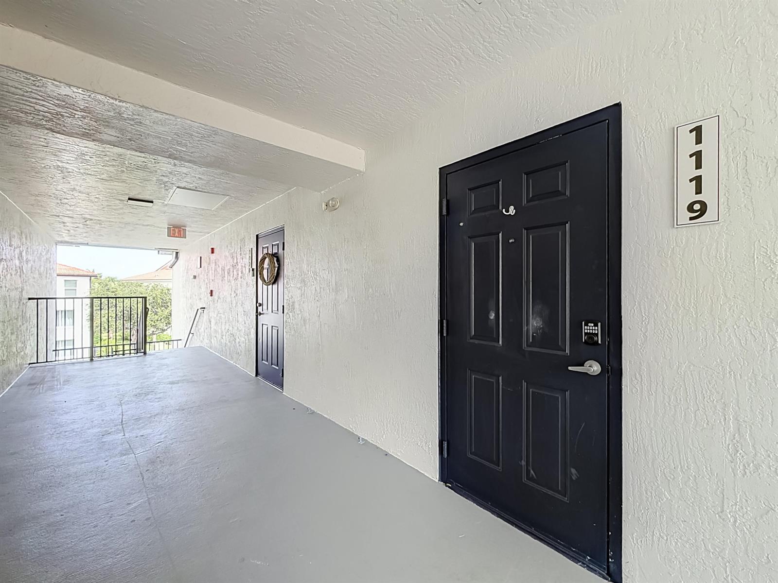A view of an outdoor apartment hallway with two black doors and unit number 1119 — 1119 Villa Lane, Boynton Beach FL 33436, BOYNTON BEACH, FL