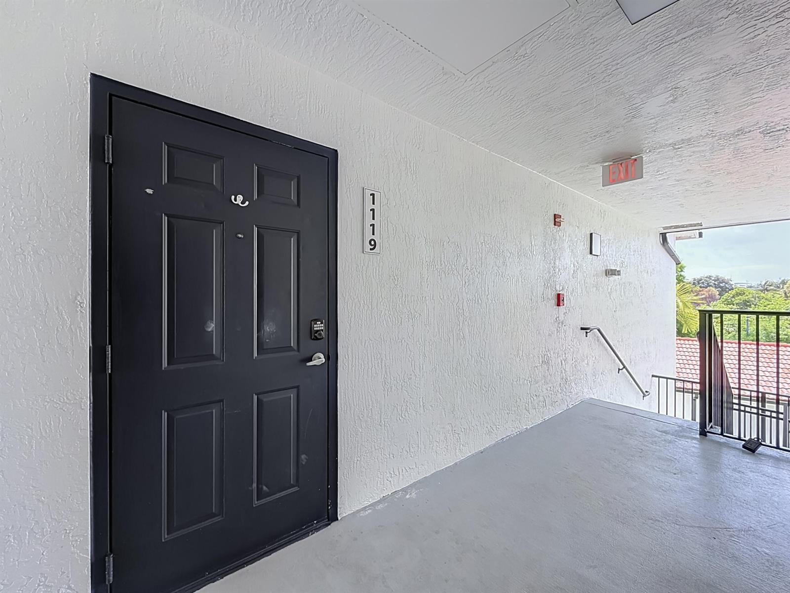 A dark door with a keypad lock is located in a white-walled outdoor hallway — 1119 Villa Lane, Boynton Beach FL 33436, BOYNTON BEACH, FL
