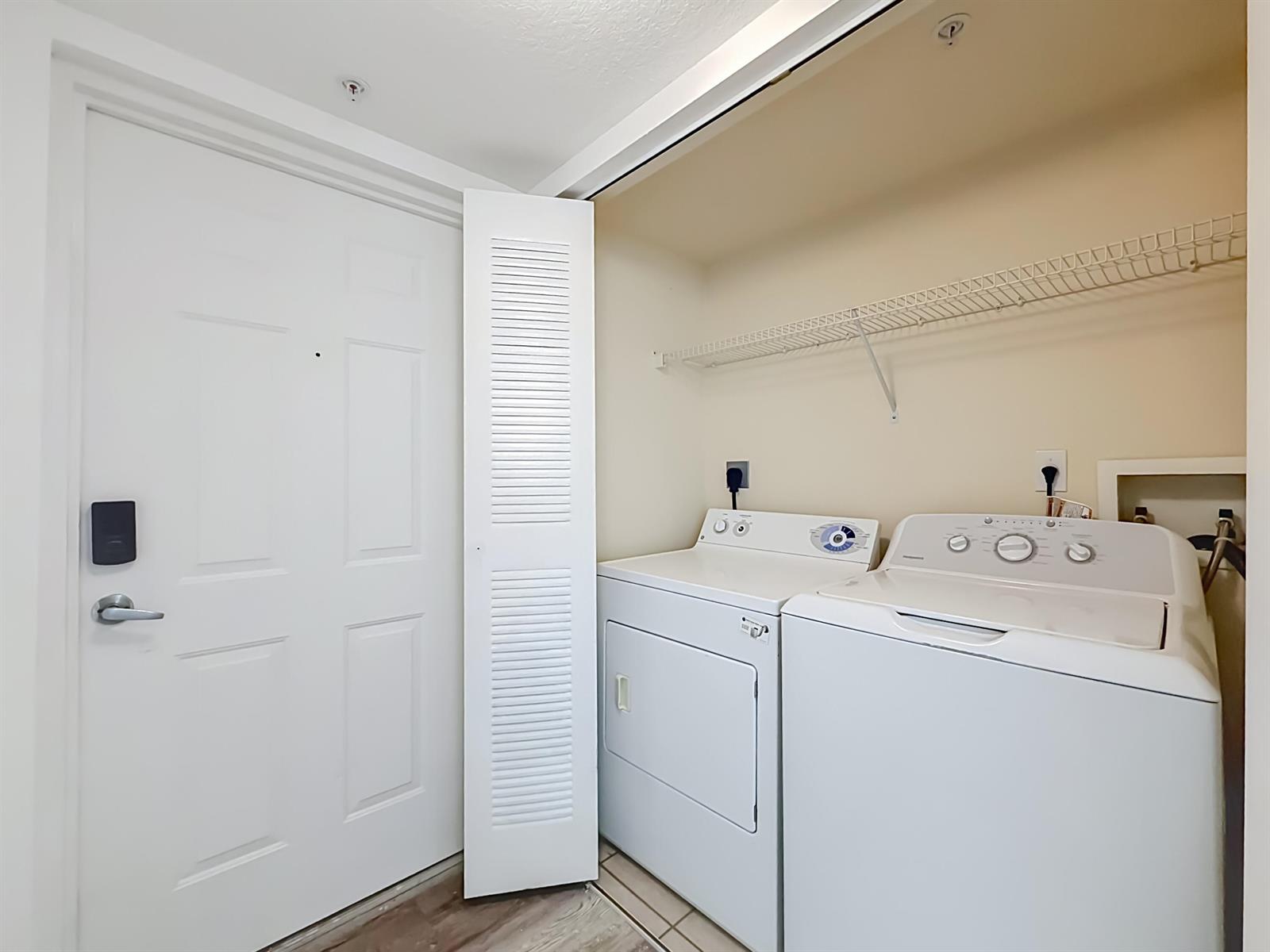 A laundry closet contains a white washer and dryer beneath a wire storage shelf — 1119 Villa Lane, Boynton Beach FL 33436, BOYNTON BEACH, FL