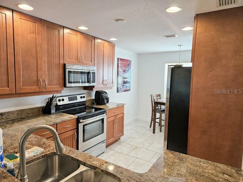 A kitchen features wood cabinets, granite countertops, stainless steel appliances, and tile flooring — 6618 7TH AVENUE CIRCLE W UNIT 1404, BRADENTON, FL