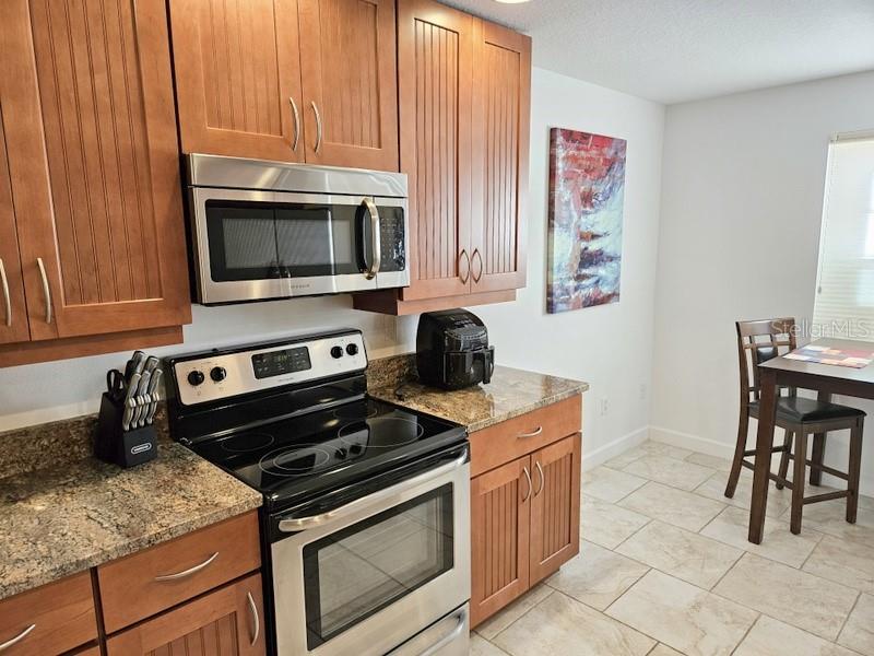 A kitchen features wood cabinets, granite countertops, stainless steel appliances, and an adjacent dining area — 6618 7TH AVENUE CIRCLE W UNIT 1404, BRADENTON, FL