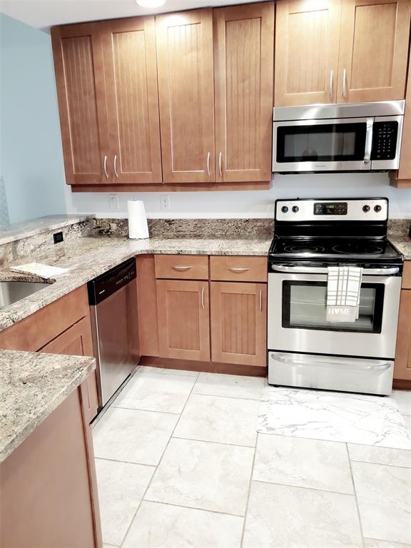 A kitchen features wood cabinets, granite countertops, stainless steel appliances, and light-colored tile flooring — 6618 7TH AVENUE CIRCLE W UNIT 1404, BRADENTON, FL