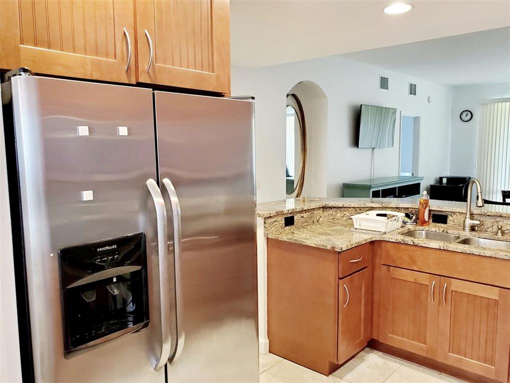 A stainless steel refrigerator stands next to a kitchen counter with granite tops and wood cabinets — 6618 7TH AVENUE CIRCLE W UNIT 1404, BRADENTON, FL
