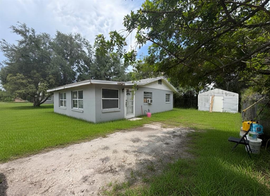 A gray single-story house with a gravel driveway and a small metal shed nearby — 3312 W 5TH STREET, SANFORD, FL