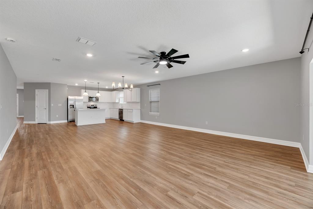 An open-concept living area features light wood-look flooring, gray walls, and a white kitchen — 9514 SUMMERS CAY CIRCLE, THONOTOSASSA, FL