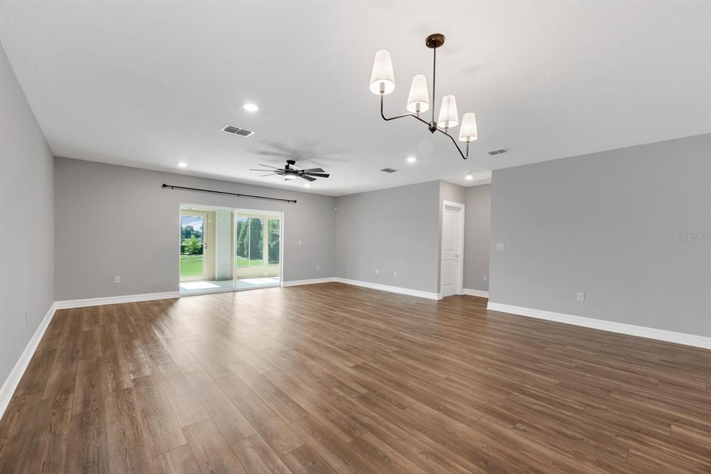 A spacious living room features light gray walls, wood-look flooring, a ceiling fan, and a chandelier — 9514 SUMMERS CAY CIRCLE, THONOTOSASSA, FL
