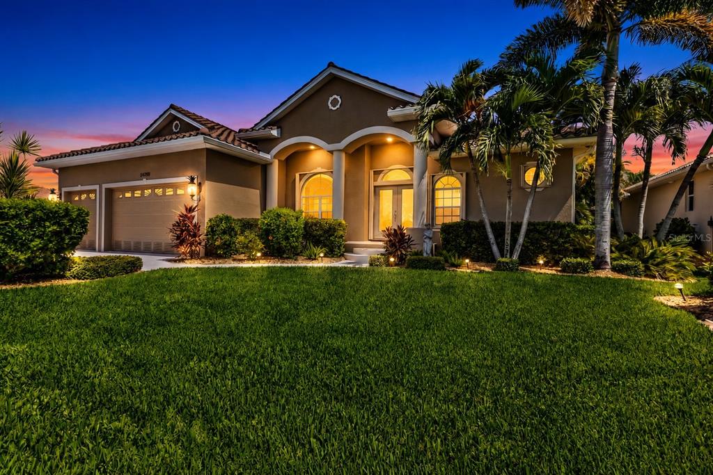 A single-story house with a tan stucco exterior, arched entryway, and palm trees at dusk — 24228 PEPPERCORN ROAD, PUNTA GORDA, FL