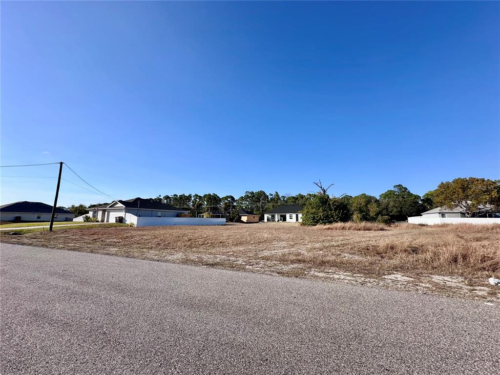 A vacant, grassy residential lot sits next to a paved road with neighboring houses nearby — 305 NE 31ST TERRACE, CAPE CORAL, FL