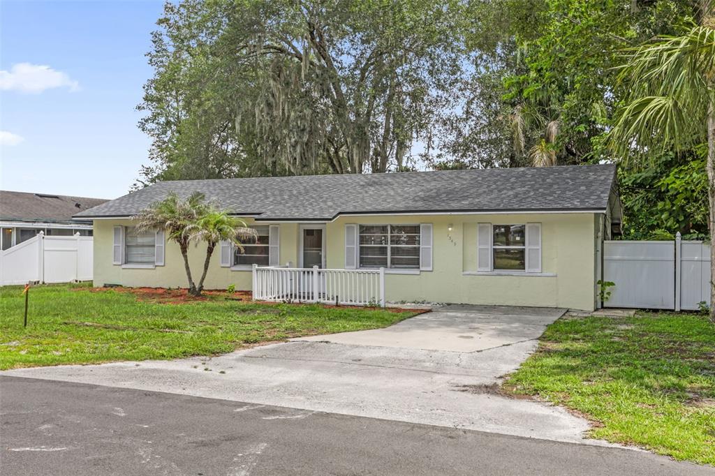 A single-story, light yellow house with a concrete driveway and a small white porch railing — 1349 E WISCONSIN AVENUE, DELAND, FL