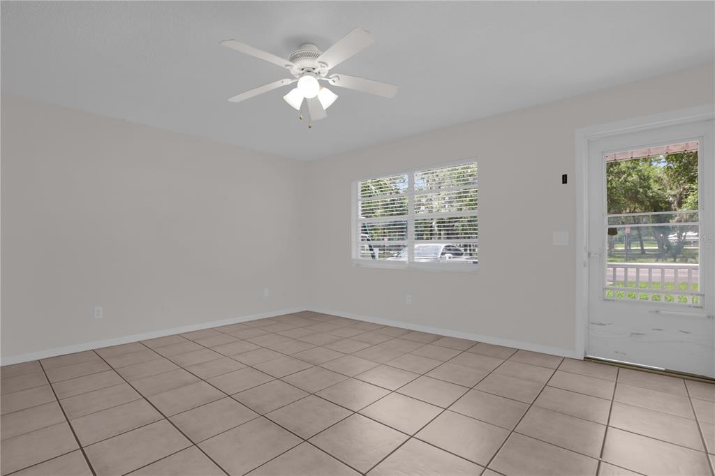 An empty room with light-colored tile flooring, a ceiling fan, and a glass-paneled exterior door — 1349 E WISCONSIN AVENUE, DELAND, FL