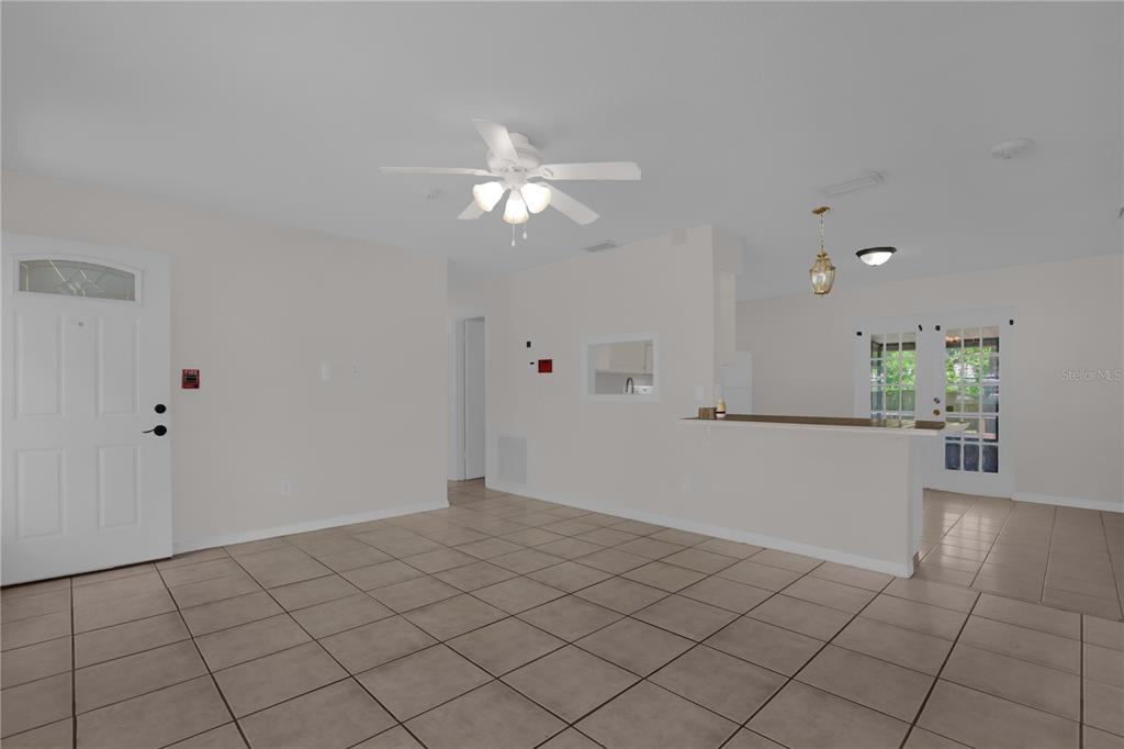 An open-concept living area features light-colored tile flooring, a ceiling fan, and a kitchen pass-through — 1349 E WISCONSIN AVENUE, DELAND, FL